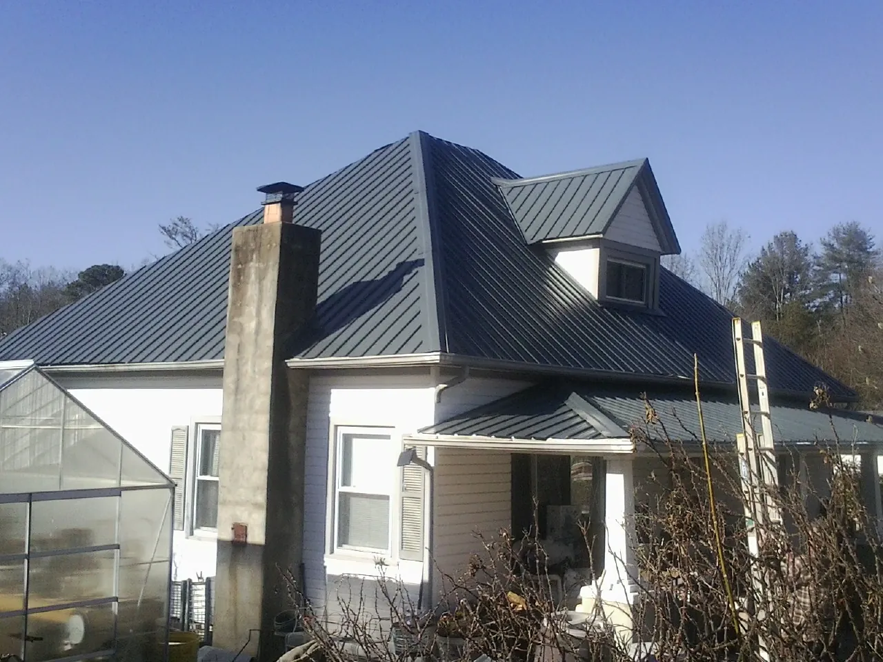 Dark blue standing seam metal roof on a white farmhouse with dormer — Slate & Tile Roof Repair by Roofing Brothers in Paulina