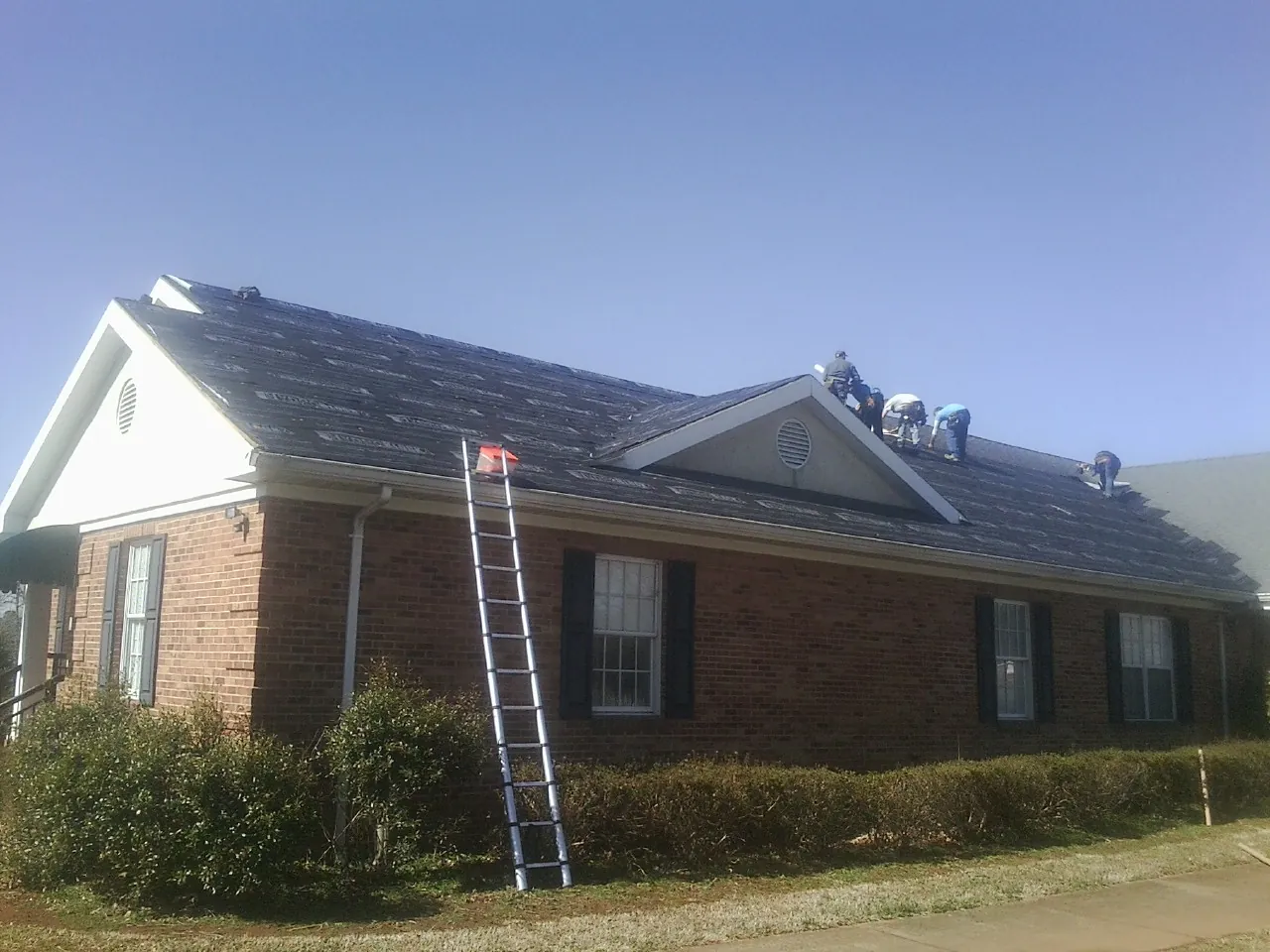 Crew tearing shingles off a brick ranch roof with a ladder set — Emergency Roof Repair work by our crew in Paulina