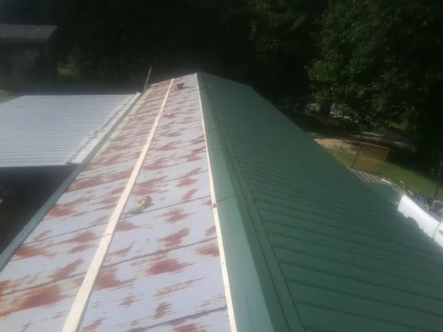 Old rusted panels beside newly installed green metal roofing — Wind Damage Roof Repair by Roofing Brothers in Paulina
