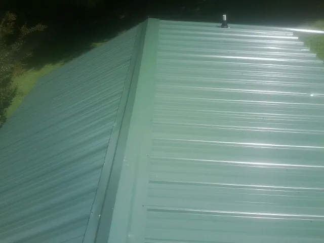 New green metal panels meeting at the ridge of a roof — Flat Roof Repair work by our crew in Paulina